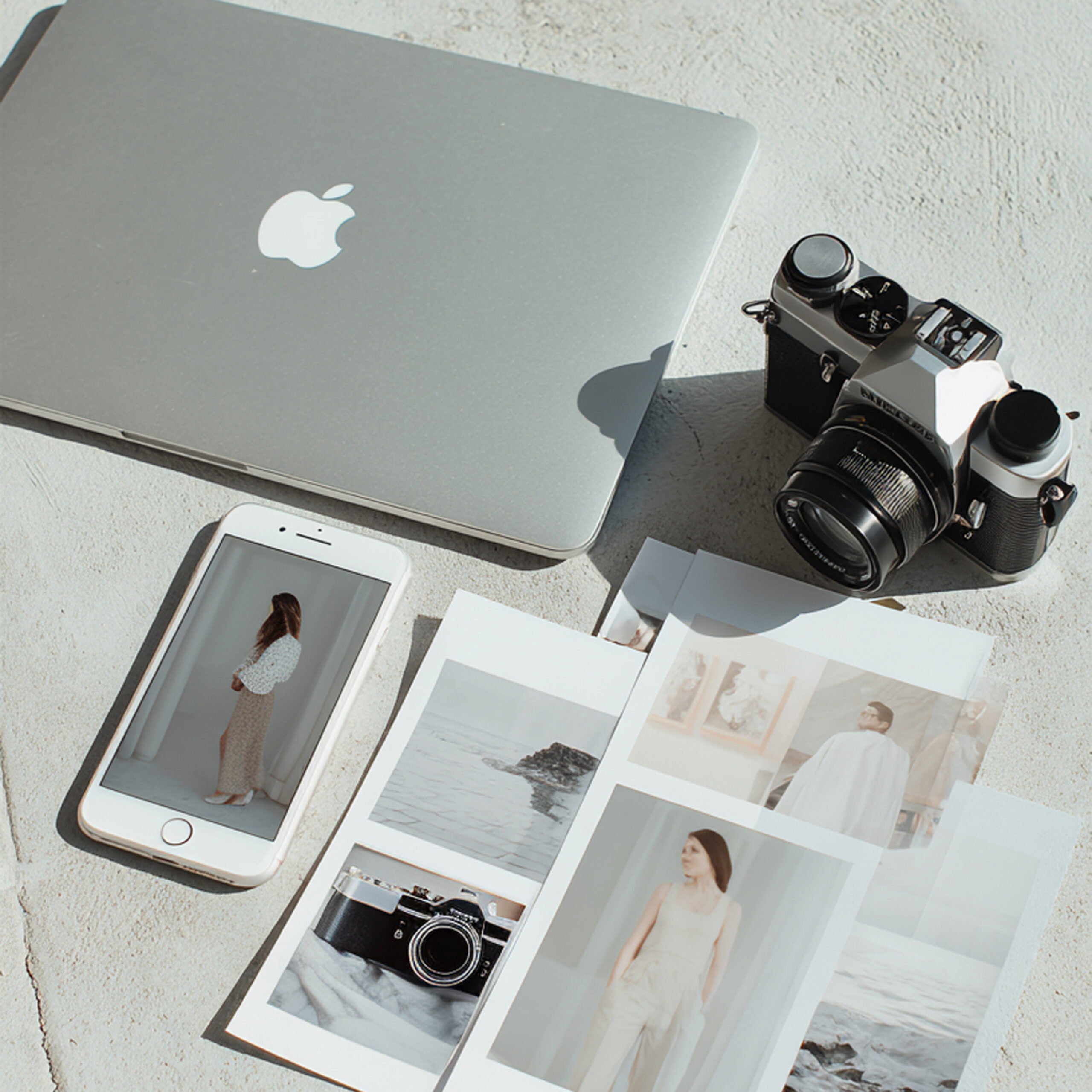 Bovenaanzicht van een dichtgeklapte MacBook, een systeemcamera, een iPhone en een verzameling lifestyle- en portretfoto's | Elena & Company