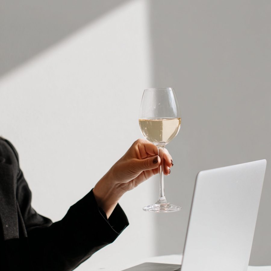 Close-up van een vrouw in een zwarte blazer die een glas champagne omhoog houdt bij haar laptop, om te toasten op een succesvolle samenwerking met haar klanten | Elena & Company